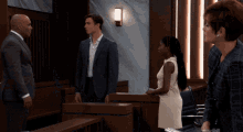 a group of people standing in a courtroom including a man in a suit and a woman in a white dress