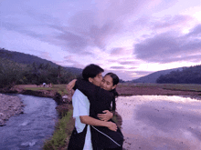 a man and a woman hugging in front of a river at sunset