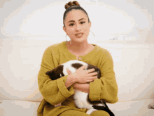a woman in a yellow sweater is holding a black and white cat in her arms