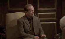 a man in a suit is sitting in a chair and talking to another man .