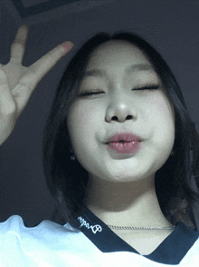 a girl making a peace sign with her eyes closed wearing a necklace that says ' barbie ' on it