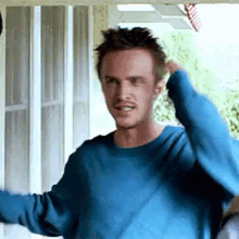 a man in a blue sweater is standing in front of a screen door .