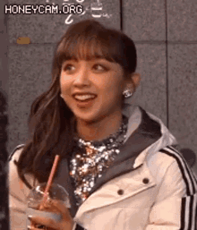 a woman in a white jacket is holding a drink with a straw and smiling .