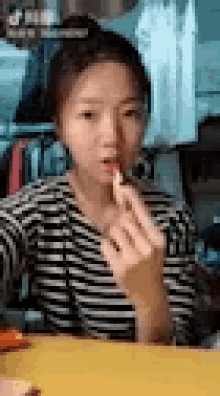 a woman in a striped shirt is sitting at a table eating a piece of food .