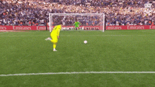 a soccer player is kicking a ball on a field with emirates advertisements behind him