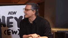 a man sitting in front of a sign that says aew hey crew
