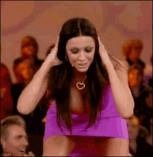 a woman in a purple dress is covering her ears with her hands .