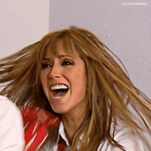 a woman is laughing with her mouth open and her hair is blowing in the wind