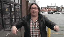 a man wearing a plaid shirt and a black jacket is standing in front of a store