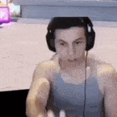 a man wearing headphones and a tank top is sitting in front of a computer screen .