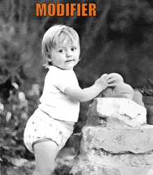 a baby in a diaper is standing on a pile of rocks with the word modifier above him