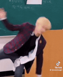 a man in a suit and tie is dancing in front of a blackboard .