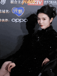 a woman in a black dress sits in front of a sign that says oppo