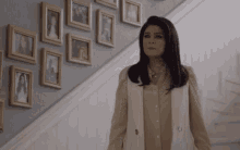 a woman in a white vest is walking down a set of stairs with pictures on the wall behind her