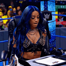 a woman with blue hair is sitting in a chair in front of a wrestling ring