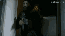 a man holding a gun in a dark room with #absentia on the bottom right