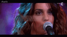 a close up of a woman singing into a microphone with #teamtal written on the bottom