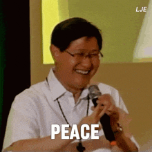 a man in a white shirt is smiling and holding a microphone with the word peace written on it