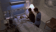 a woman is laying in a hospital bed while two men stand around her