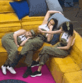 three women are laying on a yellow couch and one of them is sleeping
