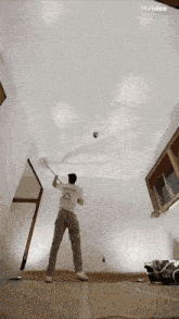 a man in a white shirt with a triangle on it is painting a ceiling