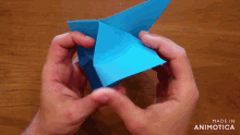 a person is holding a blue origami object with the words made in animatica on the bottom