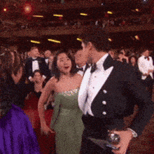 a man in a tuxedo holds a trophy in front of a woman in a green dress