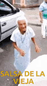 an elderly woman is dancing in front of a car with the words salsa de la vieja written below her