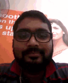 a man with glasses and a beard looks at the camera in front of a sign that says ' root ' on it