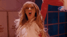 a woman with long blonde hair is wearing a feathered coat