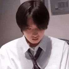 a young man wearing a white shirt and purple tie is looking down .