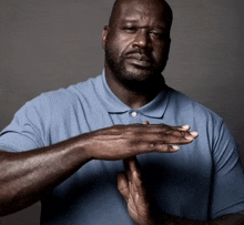 a man in a blue shirt holds his hands together in front of his face