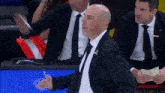 a bald man in a suit and tie stands in front of a crowd