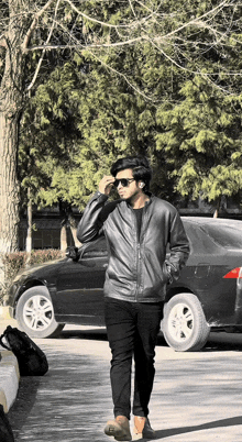 a man wearing sunglasses and a leather jacket walks down a street