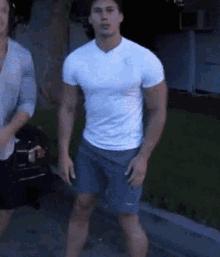 a man in a white t-shirt and blue shorts is standing on a sidewalk .
