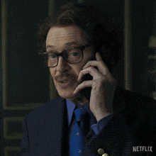 a man wearing glasses and a blue tie is talking on a cell phone with a netflix logo behind him