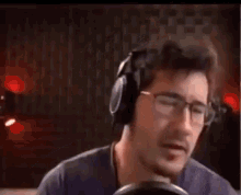 a man wearing headphones and glasses is singing into a microphone while making a funny face .