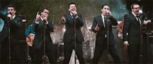a group of men in suits and ties are singing into microphones on a stage .