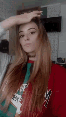 a woman with long hair is wearing a red shirt with the letter m on it .
