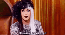 a drag queen wearing a black and white wig and a silver dress is talking .