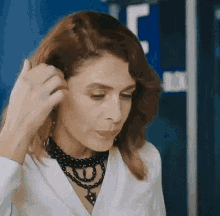 a woman in a white shirt and black necklace is adjusting her hair .