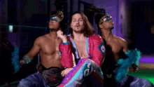 a man in a pink and purple outfit is surrounded by two men wearing masks