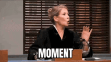 a female judge is giving a speech in front of a microphone in a courtroom and the words moment are visible .