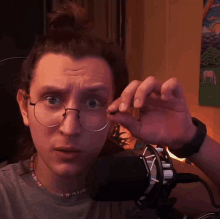 a man wearing glasses stands in front of a microphone and looks surprised