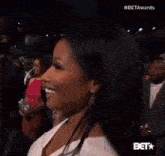 a woman in a white dress is smiling while standing in front of a crowd at a bet awards event .