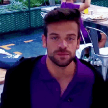 a man with a beard wearing a purple shirt is looking at the camera .