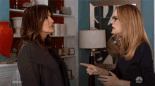 two women are having a conversation in a living room and one is pointing