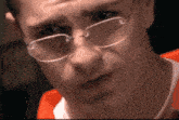 a man wearing glasses looks at the camera with a serious look on his face