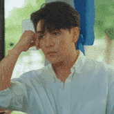 a young man in a white shirt is sitting on a bus with his hand on his face .