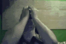 a person is covering their face with their hands while sitting in front of a green wall .